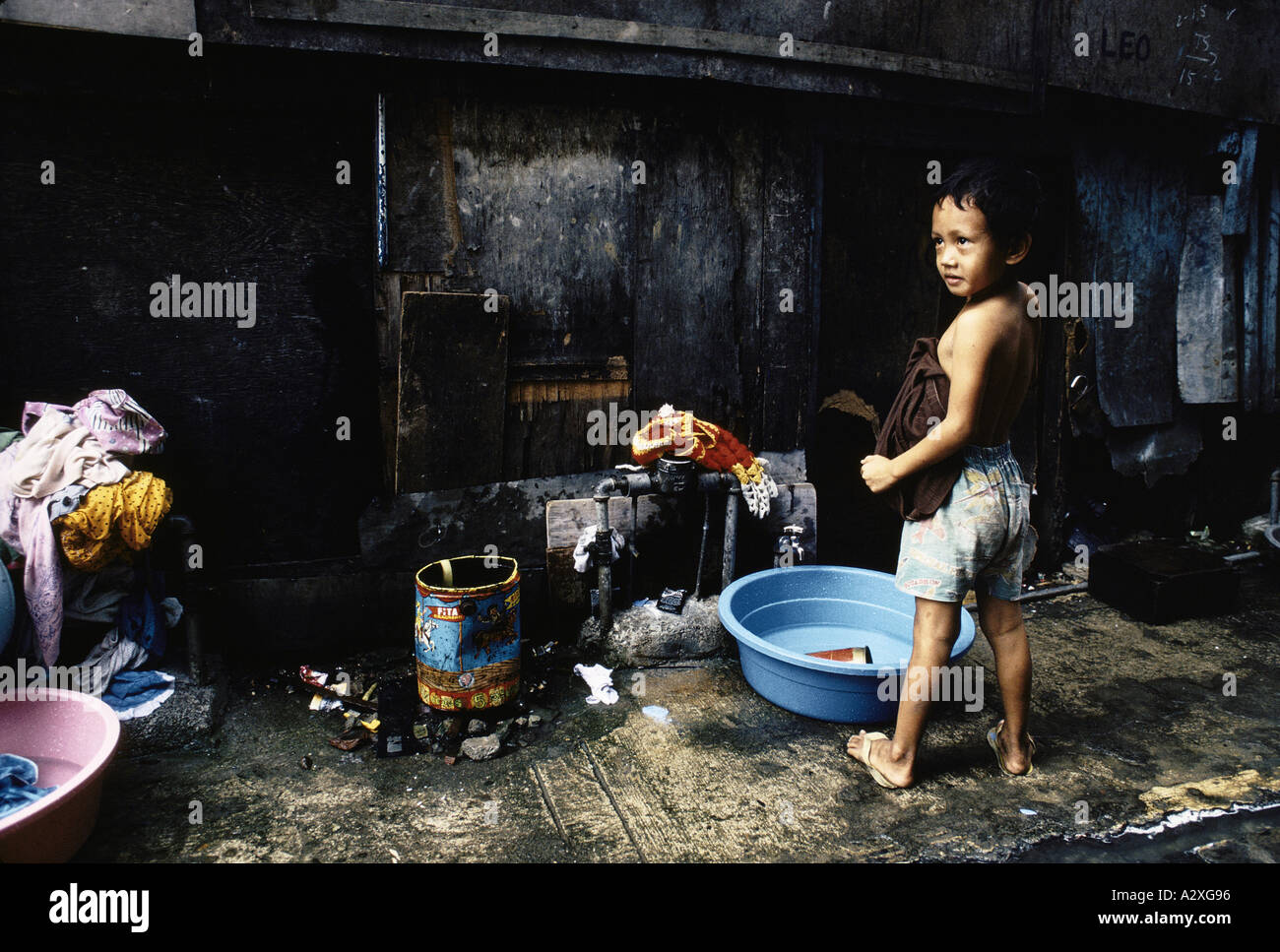 Philippines  - a young boy  stands beside a bowl of water to help his mother with the washing in a Manila slum , Feb 1991 Stock Photo