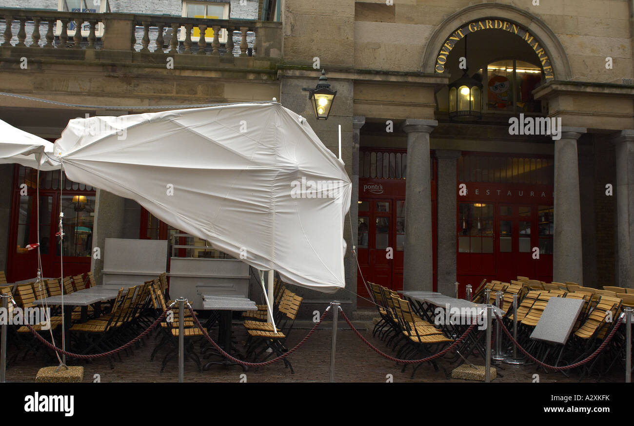Strong wind blowing outdoors chairs and parasols at cafe in Covent Garden London Stock Photo