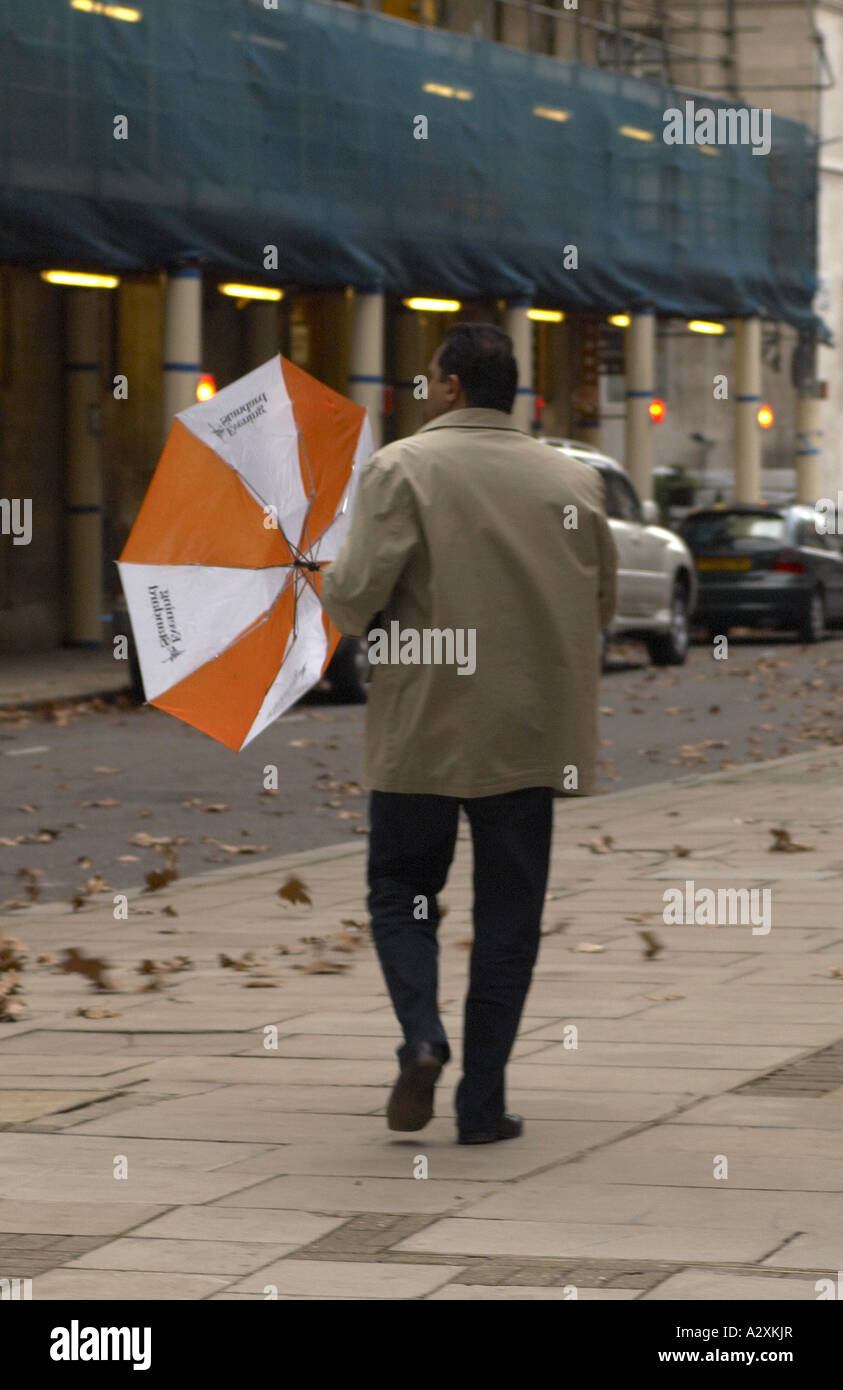 Man with Evening Standard umbrella walking in strong wind London Stock Photo