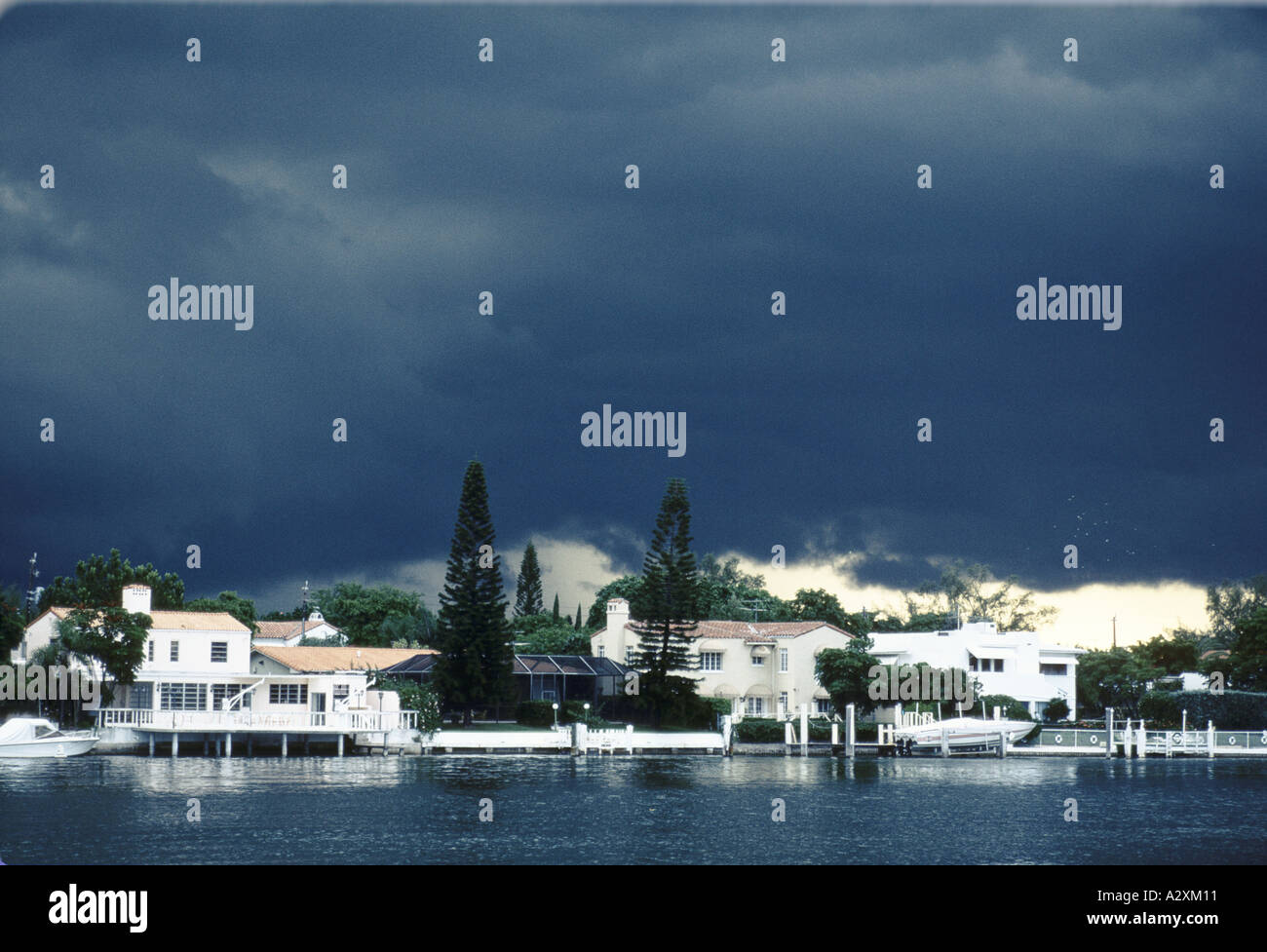 dark heavy clouds hover over elegant expensive looking homes that are next to flat but dark water during a hurricane in miami Stock Photo
