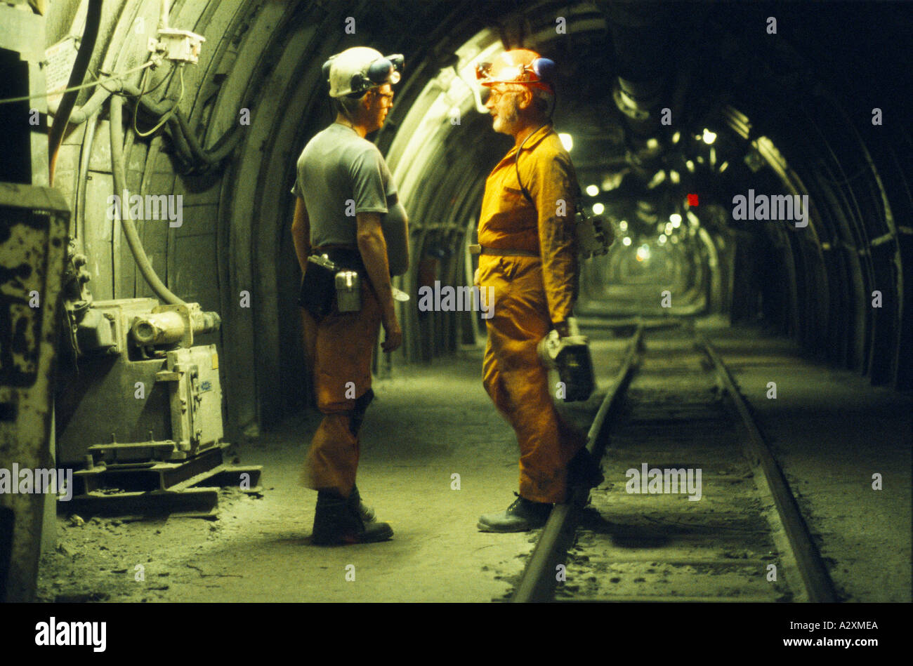 MINERS WITH SAFETY HELMETS & HEAD TORCH CHATTING IN UNDERGROUND TUNNEL WITH RAIL TRACKS. SHIREBROOK COLLIERY, NOTTINGHAMSHIRE. Stock Photo