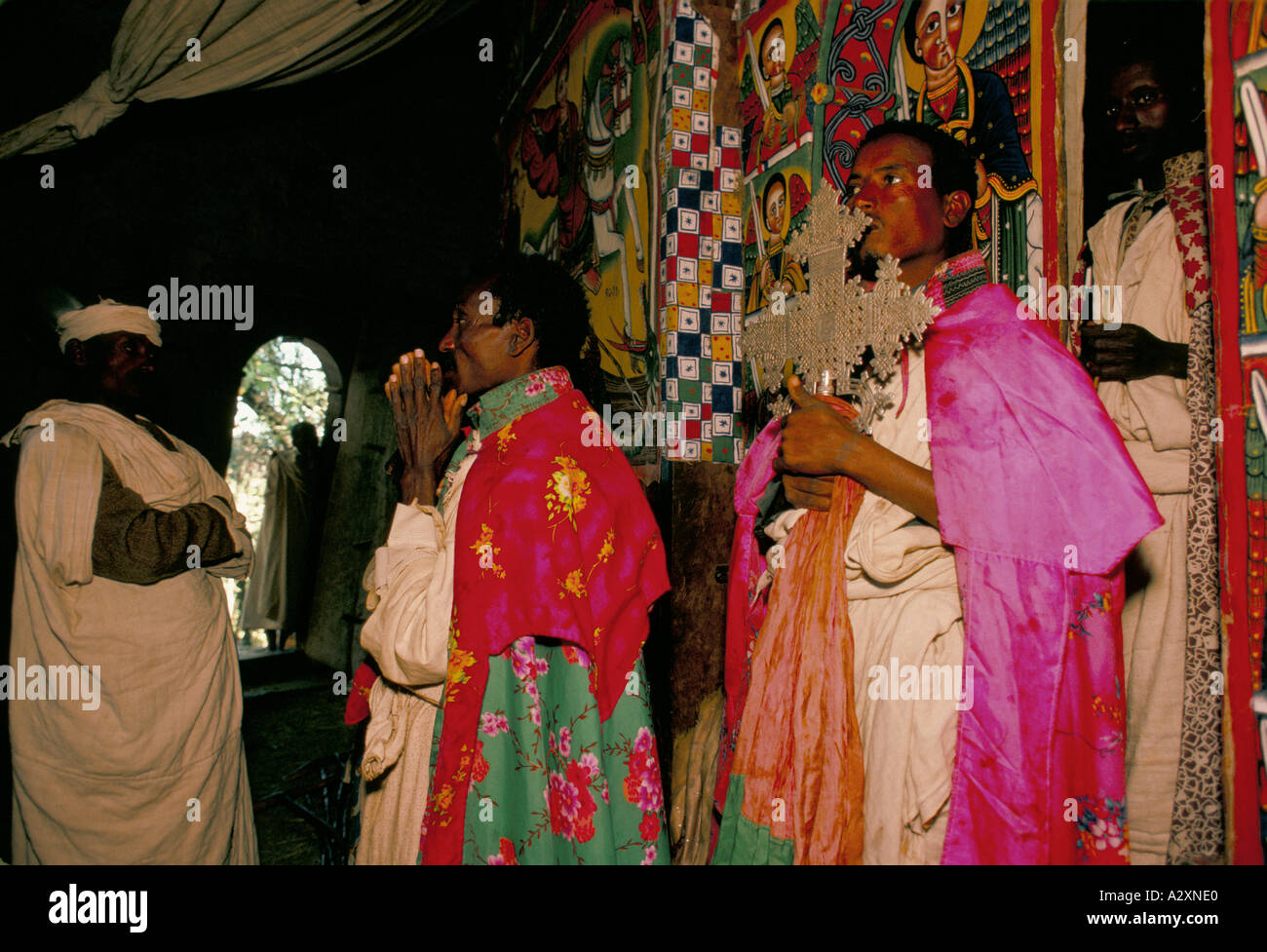 religious wall hangings man wearing pink green robes holding ornate silver cross praying at church service tigray Stock Photo