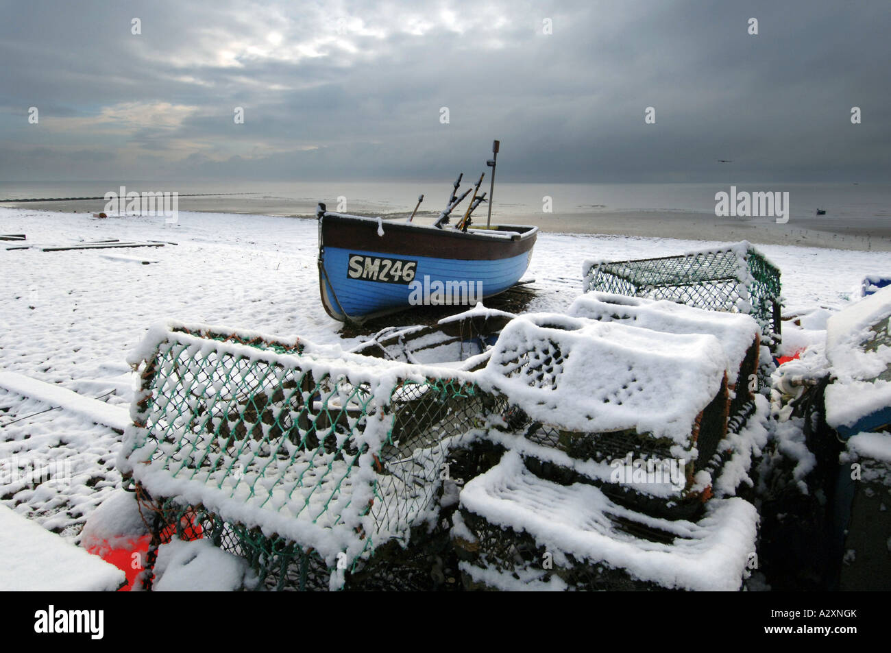 Snow on a solitary fishing boat and a pile of lobster pots on Worthing beach after winter storms in Sussex and Kent Stock Photo