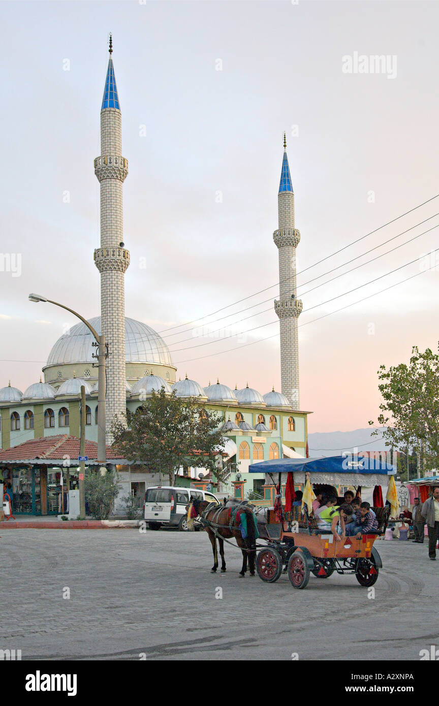 A horsedrawn carriage on the street with mosque minarets at sunset in the village of Karahayit, Turkey Stock Photo
