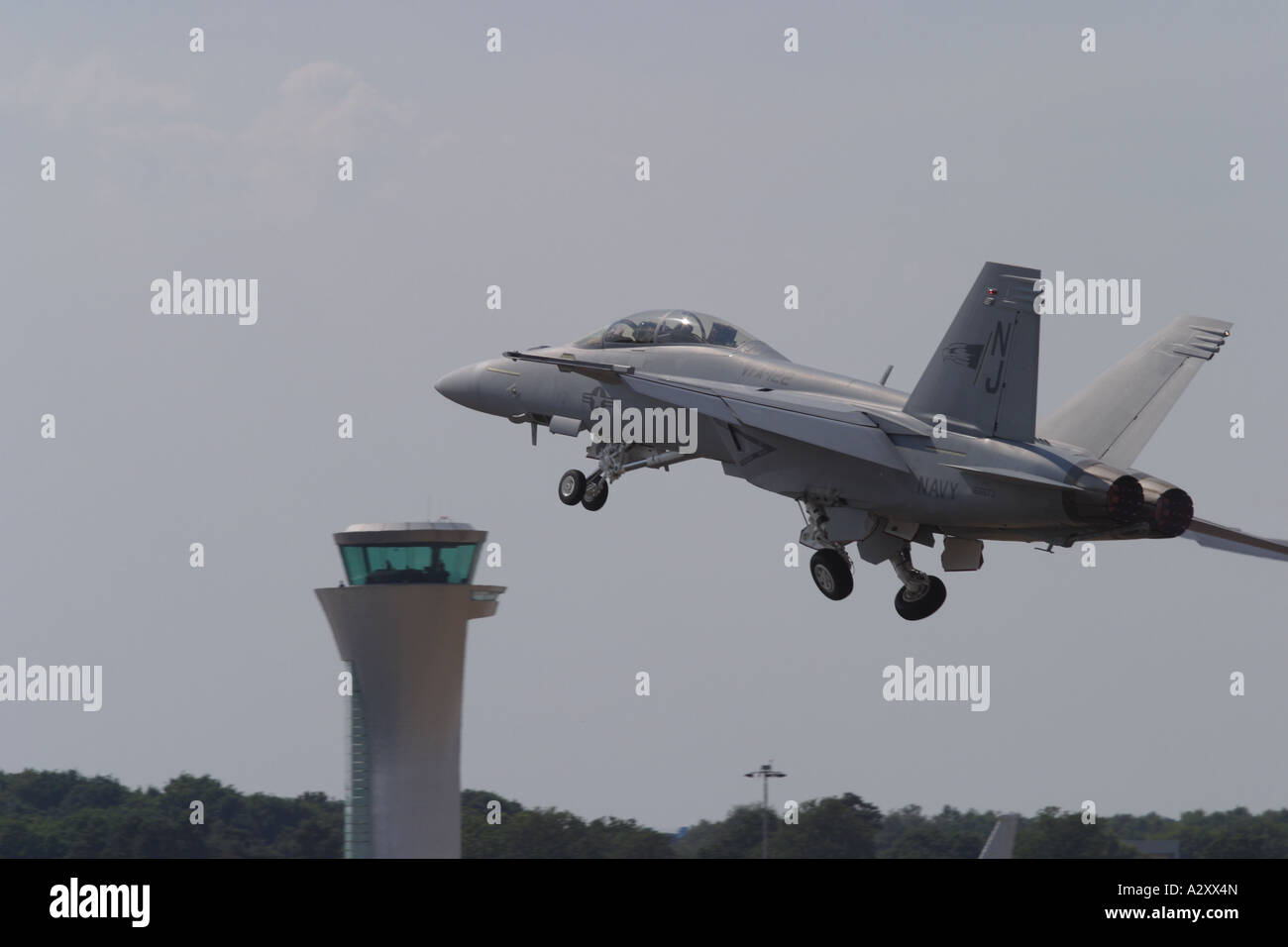 US Navy F-18F Hornet strike fighter taking off with airport air traffic control tower Stock Photo