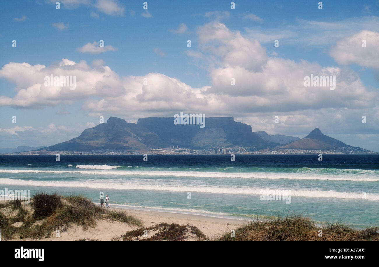 A couple walk on the beach with Capetown and Table Mountain and Lions Head in the background South Africa Stock Photo