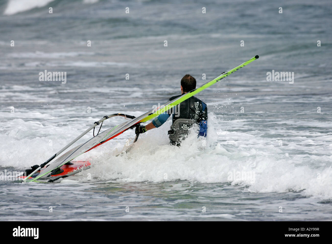 male windsurfer in wetsuit drags his board and sail through the waves in the sea off El Medano beach Tenerife Canary Islands Stock Photo