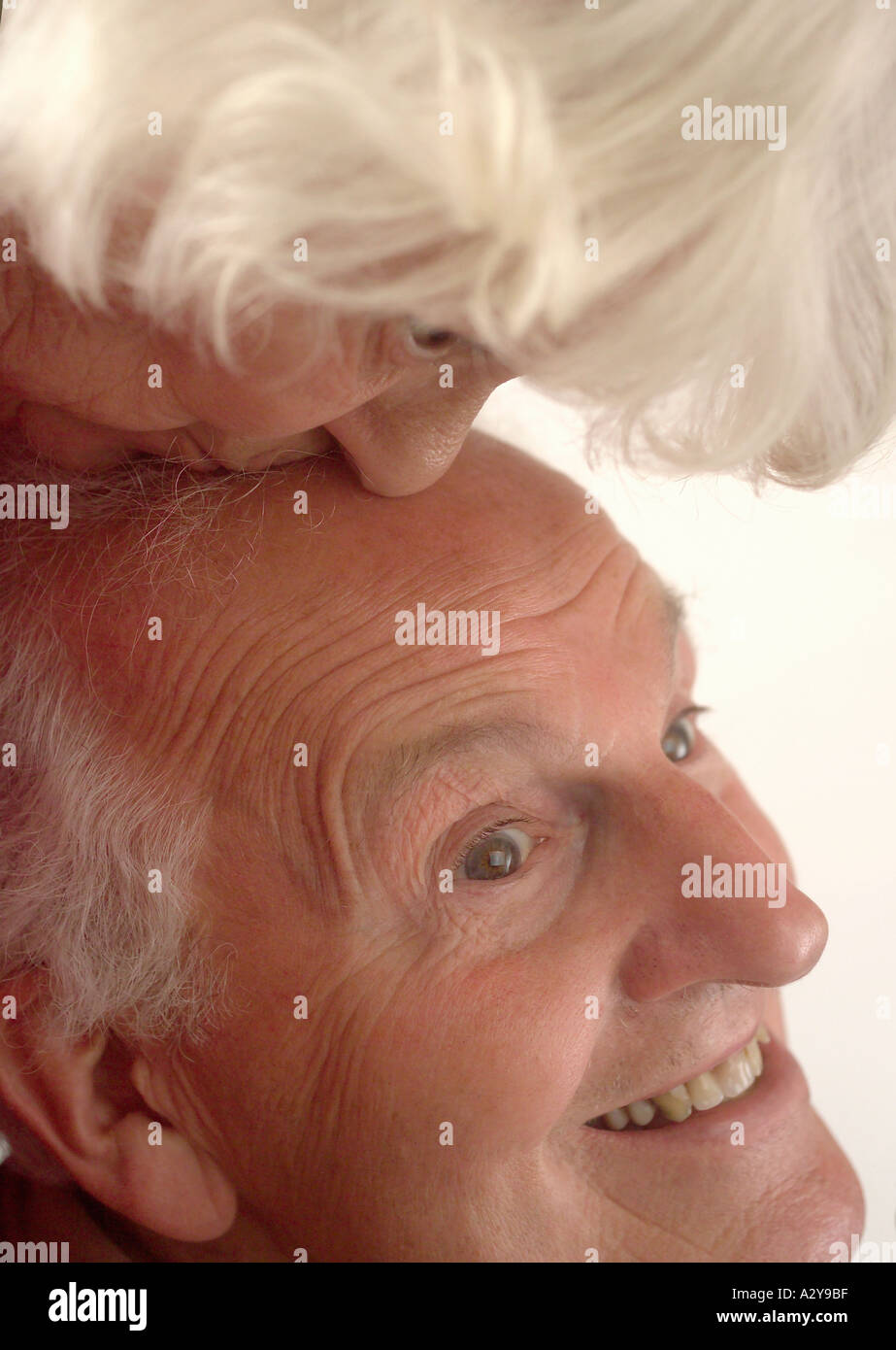 Woman kissing smiling old man on bald head Stock Photo