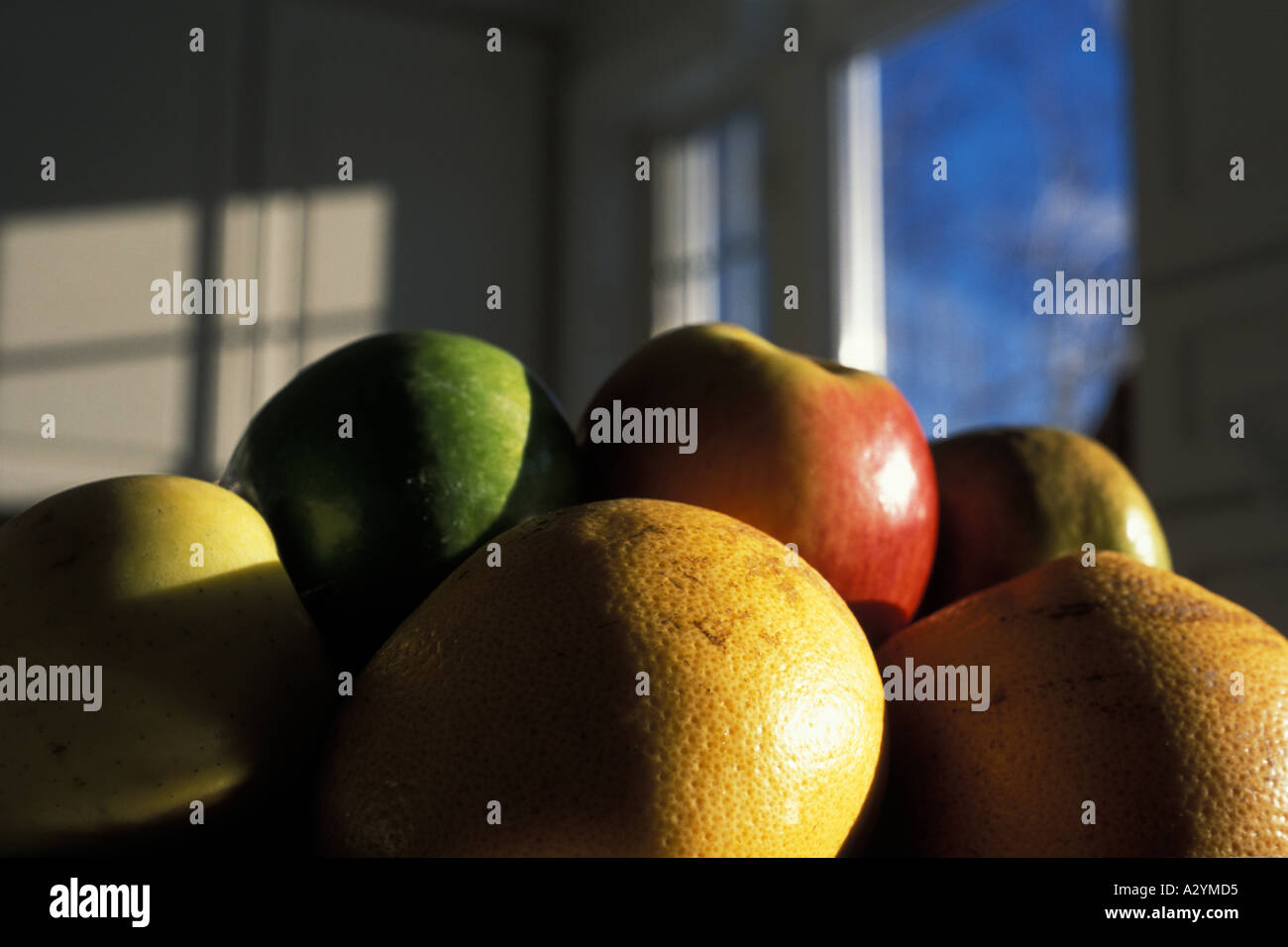 Oranges and apples in a fruit bowl with sunset light on them and a blue sky through a window showing in the background Stock Photo