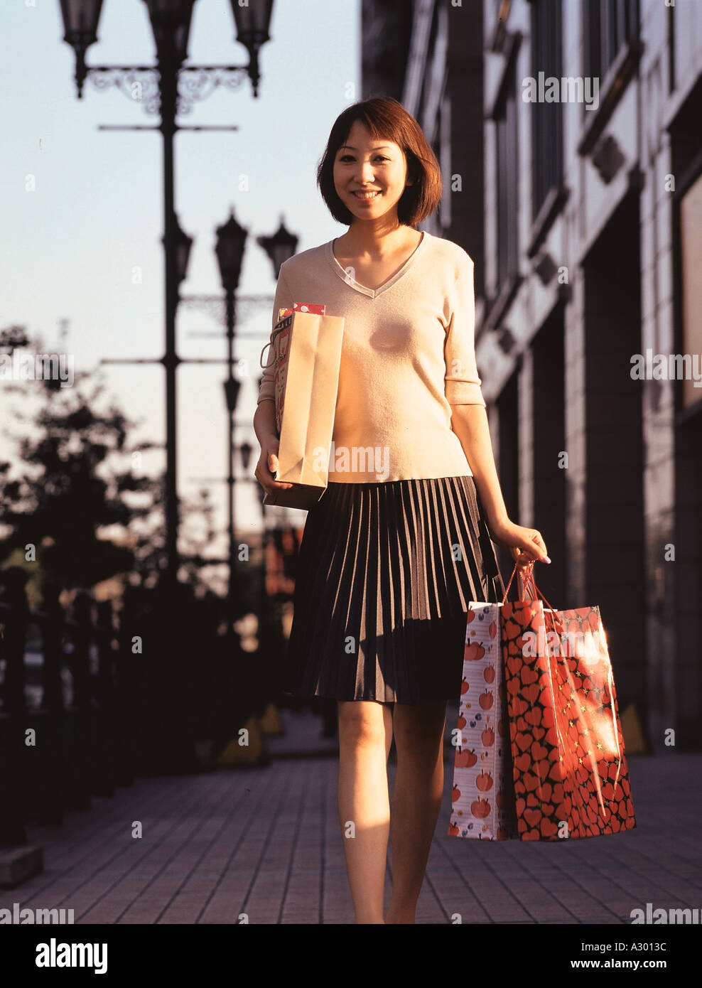 a chinese young woman holding shopping bags walking along the street Stock Photo