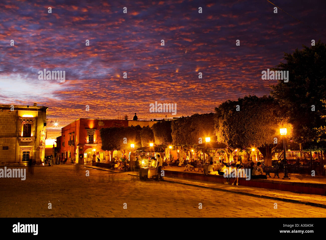 MEXICO San Miguel de Allende Sunset sky over Jardin Principal street vendors and people sitting under trees Stock Photo