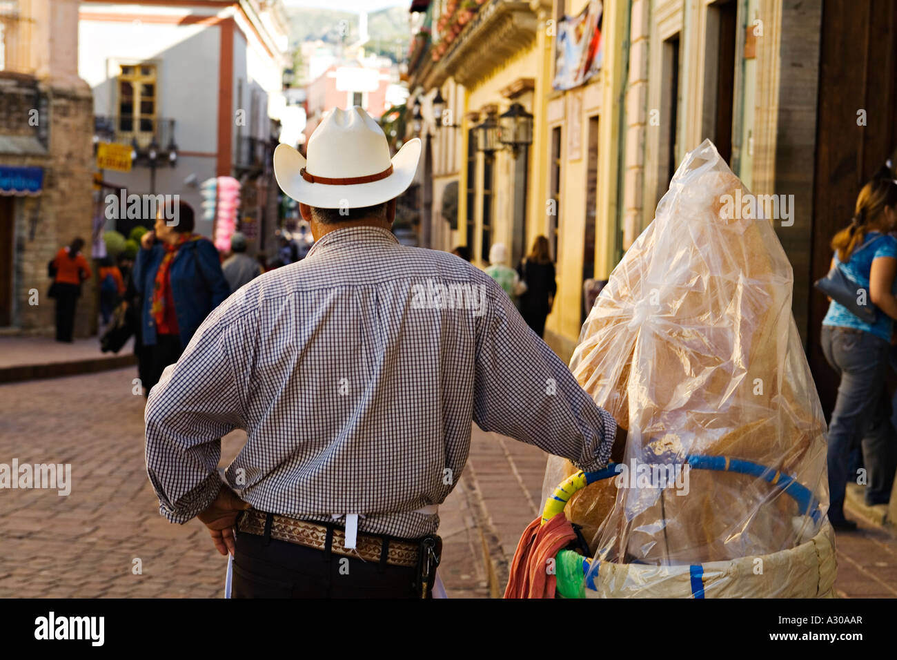 MEXICO Guanajuato Mexican man wearing cowboy hat stand next to large churro, busy city pedestrian area Stock Photo
