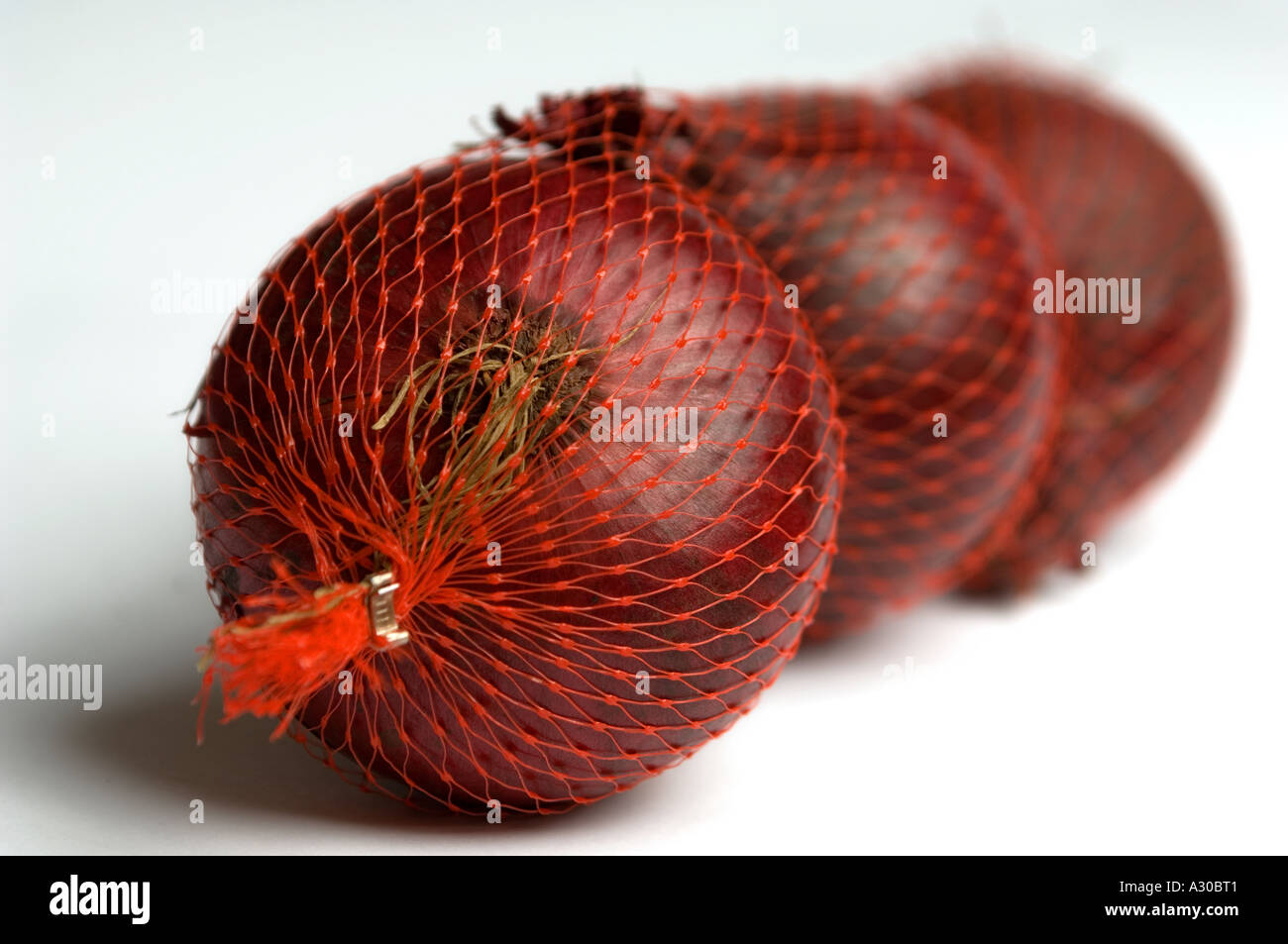 Red Onions in mesh bags against white studio background Stock Photo