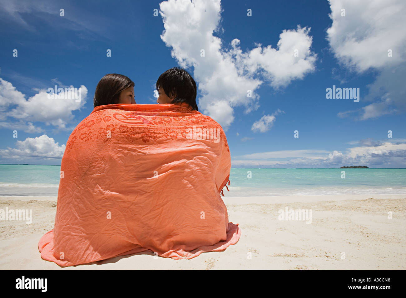 Couple wrapped in shawl on beach Stock Photo