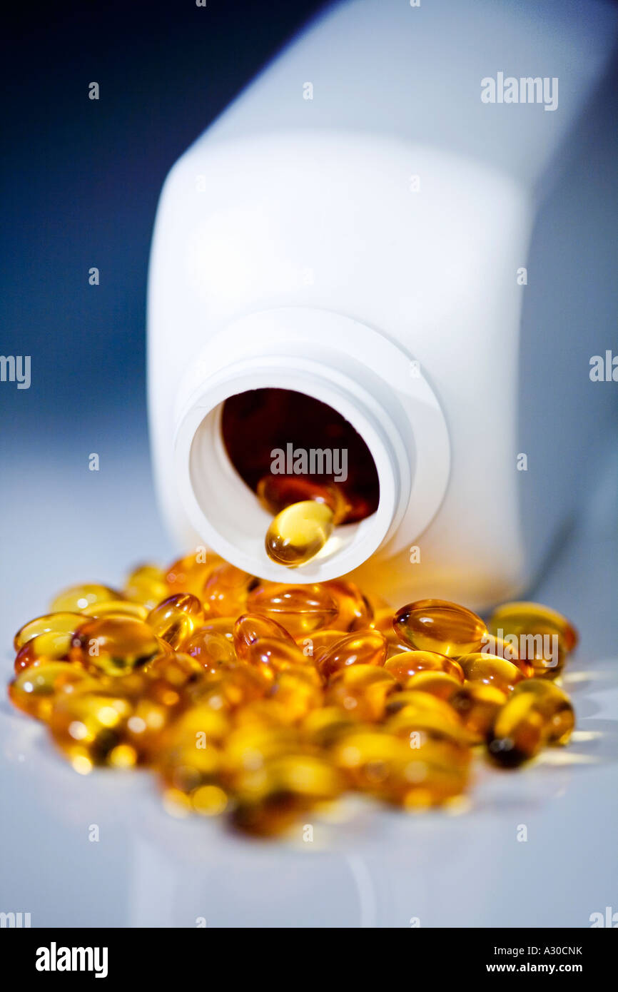 Bottle of yellow shiny pills spilled onto shiny surface Stock Photo