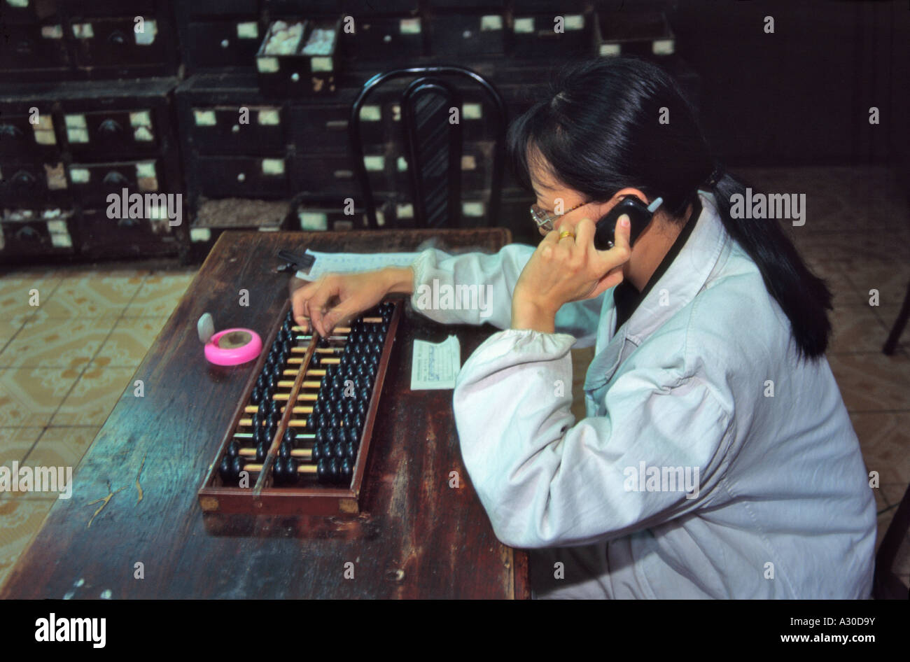 Woman using traditional abucus and modern cellular phone in Chinese medicine pharmacy Wanxian Chongqing China Stock Photo