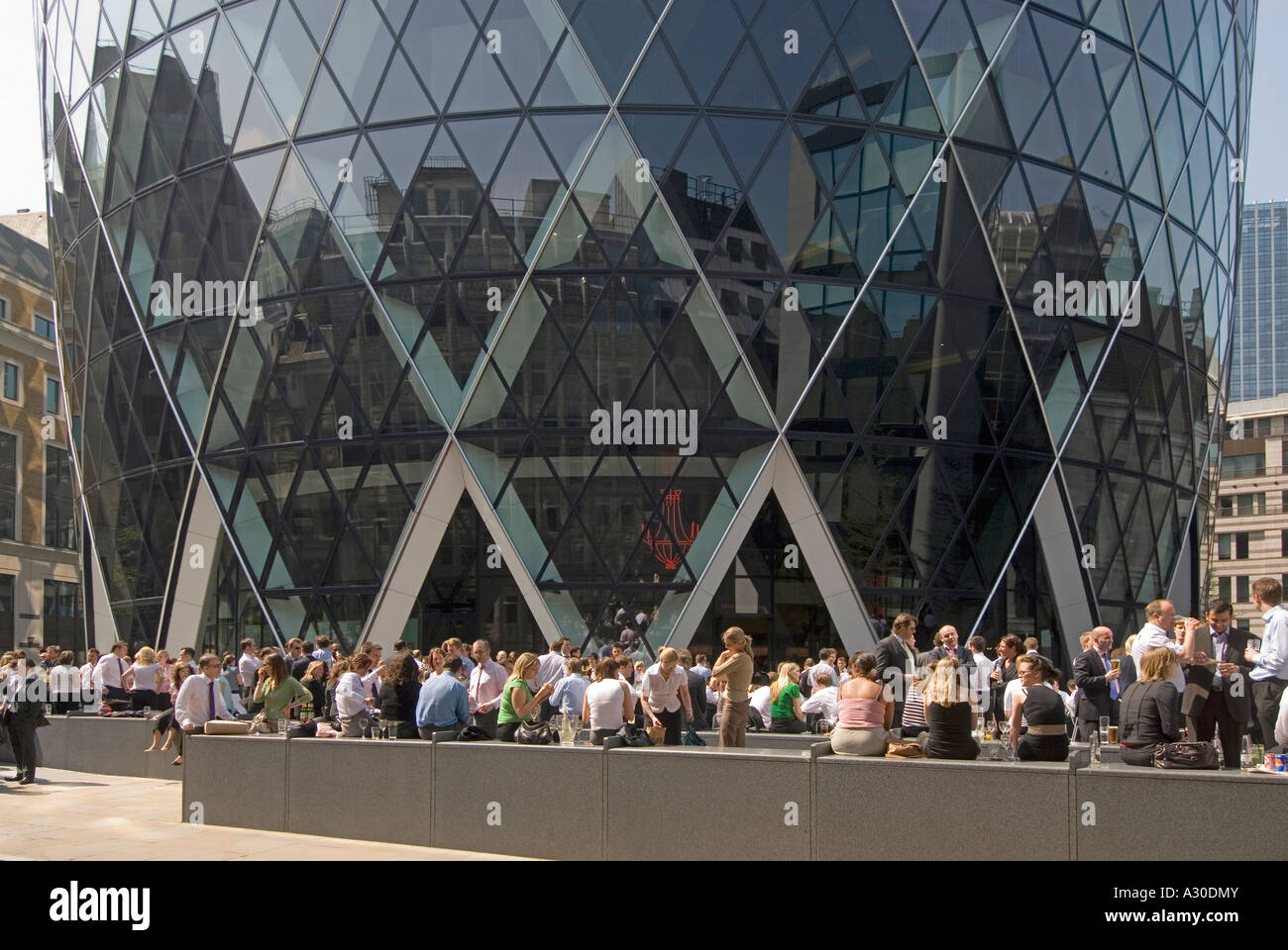 City of London close up of base of Gherkin building with office workers outdoors lunchtime lifestyle on a hot summers day England UK Stock Photo