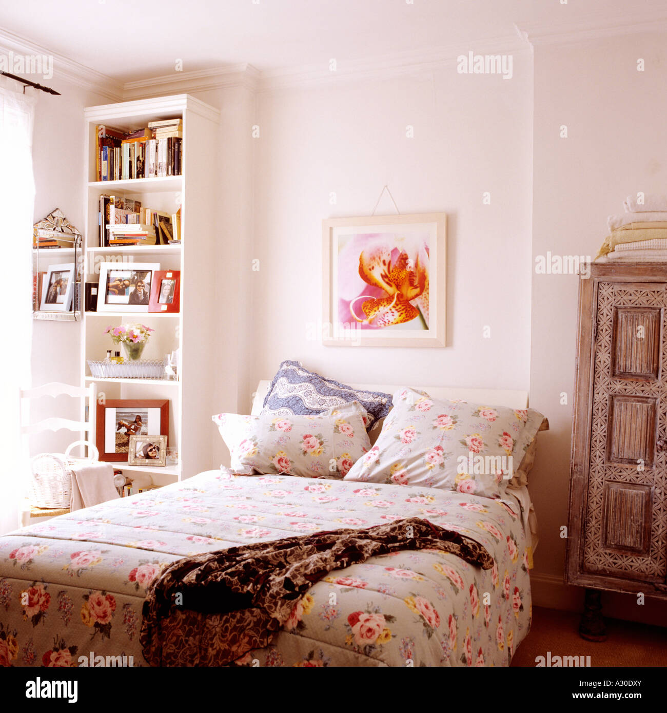 Floral patterned bed cover on queen sized bed under artwork with bookcase Stock Photo