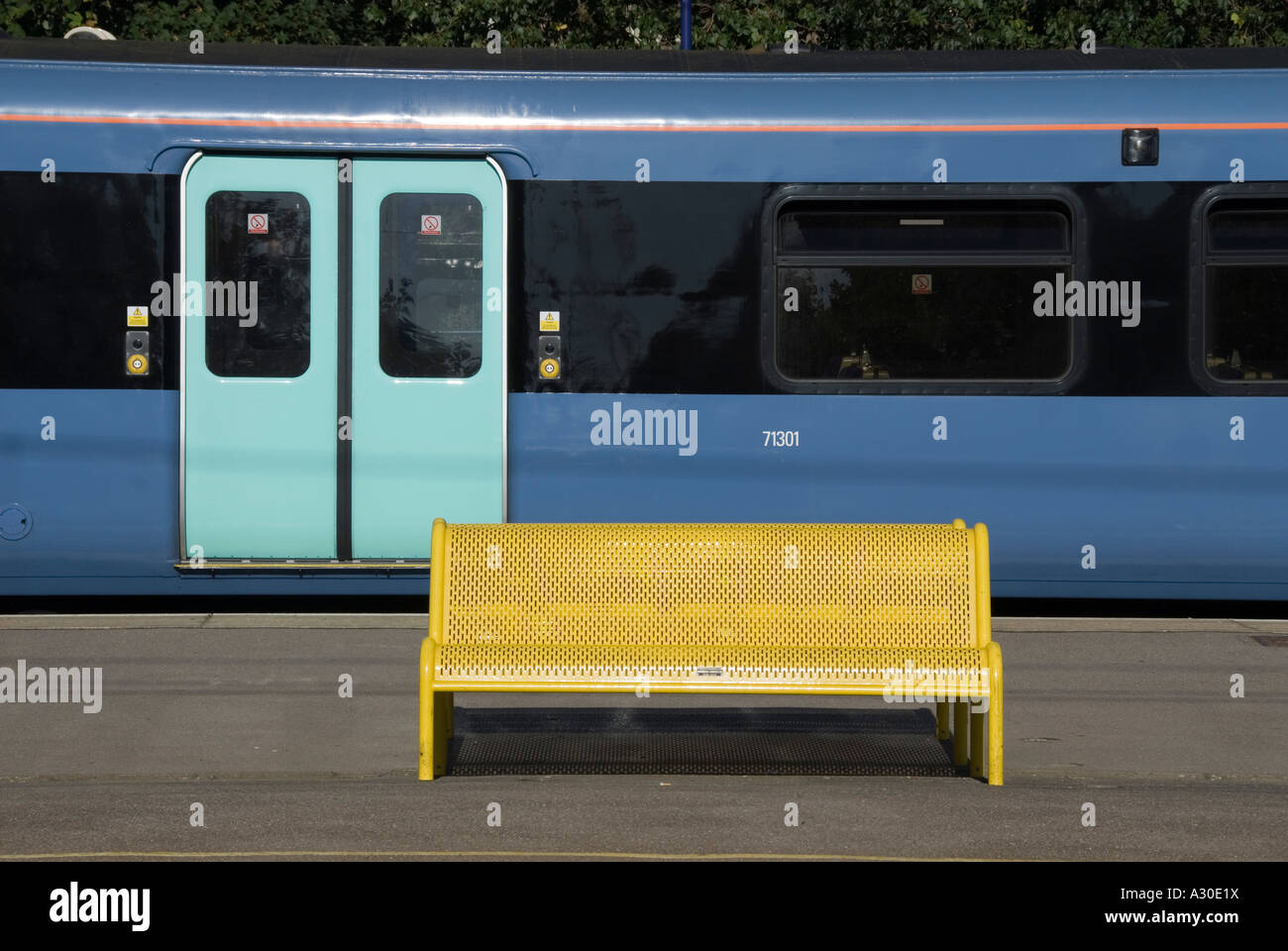Train station platform seat painted bright yellow contrasted with colours & shapes of public transport railway passenger carriage Essex England UK Stock Photo
