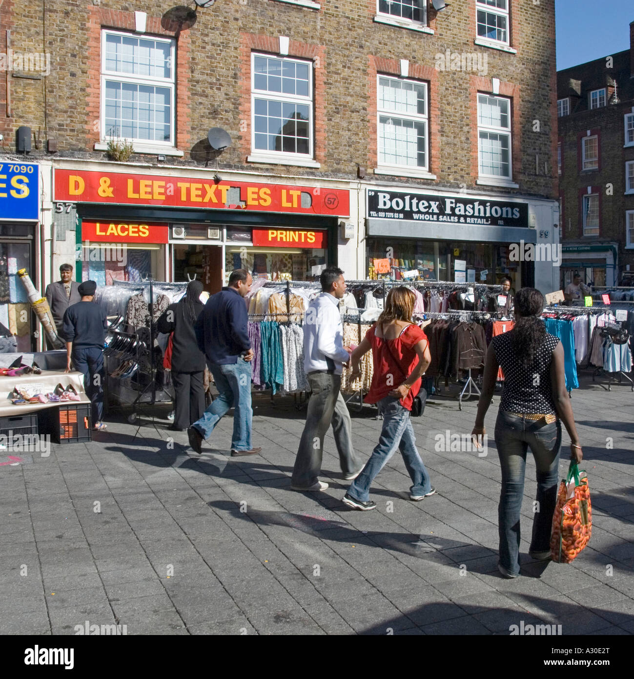 Shoppers in Wentworth Street part of Petticoat Lane Market with  clothing rails outdoors on pavement in front of retail business shop front London UK Stock Photo