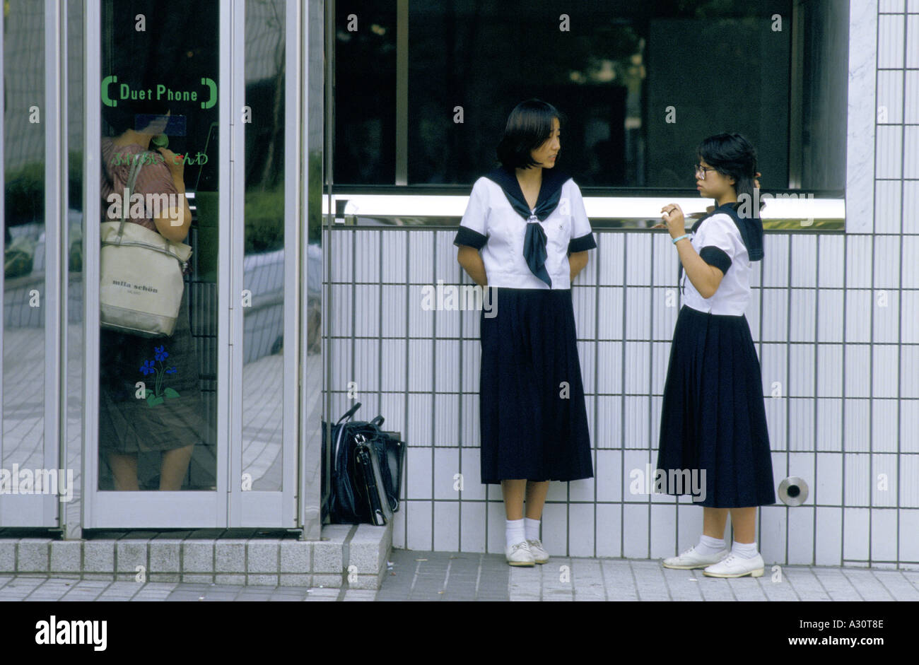 tokyo japan two school girls wait to use a new phone booth with a duet phone which has two handsets Stock Photo