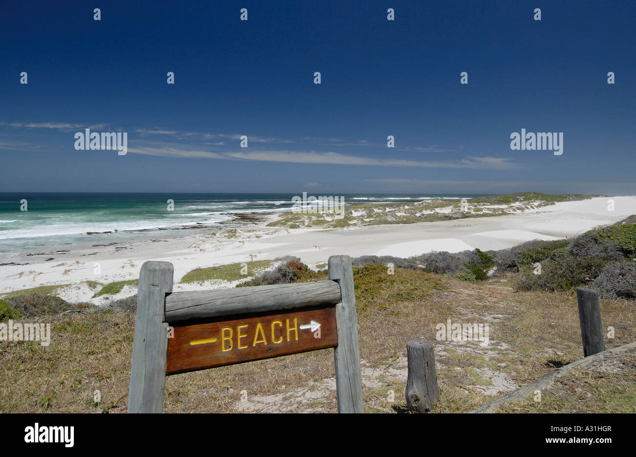 A wooden sign saying Beach pointing to an expanse of silver sand and blue ocean with no people present Stock Photo