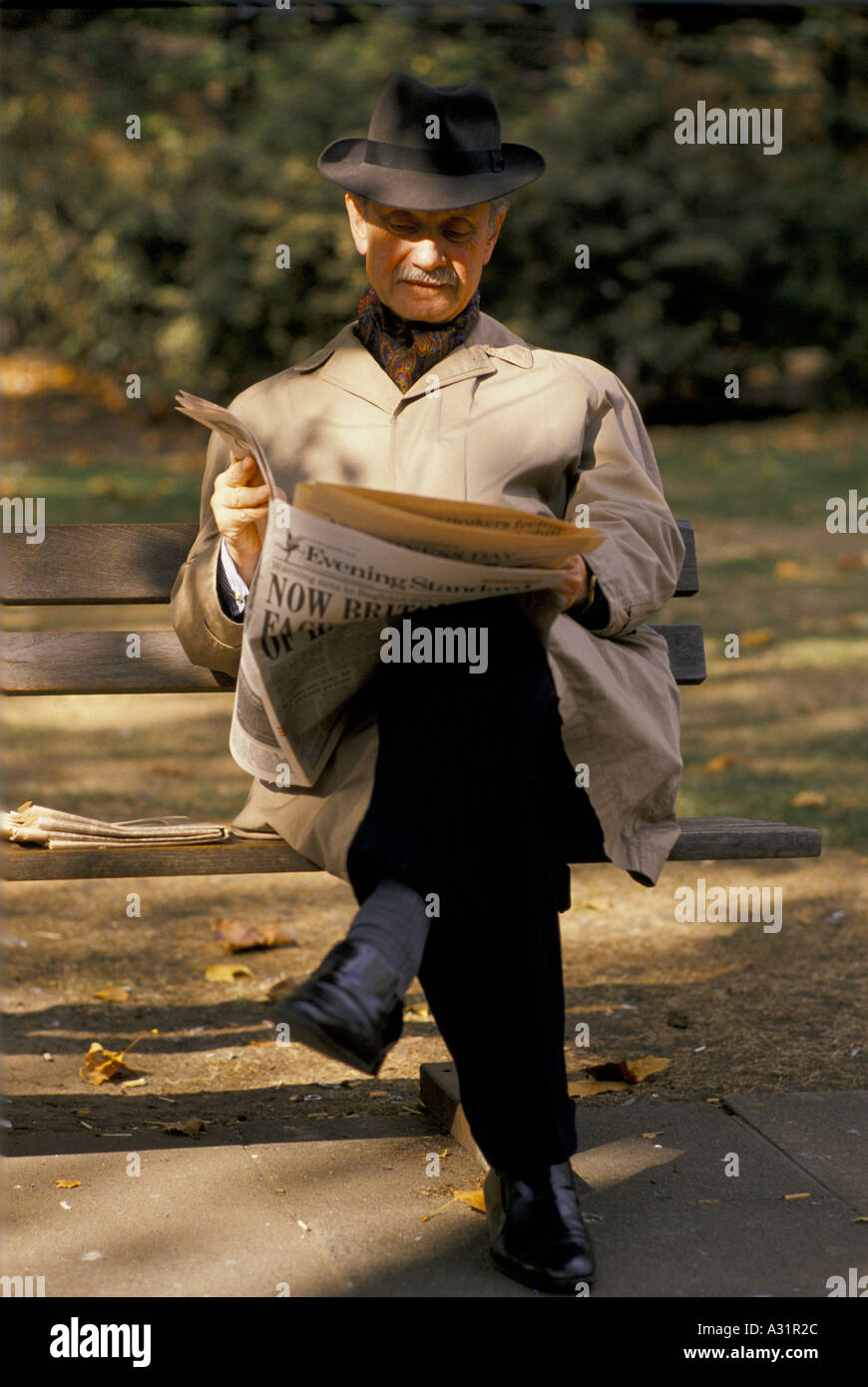 man reading evening standard on park bench Stock Photo
