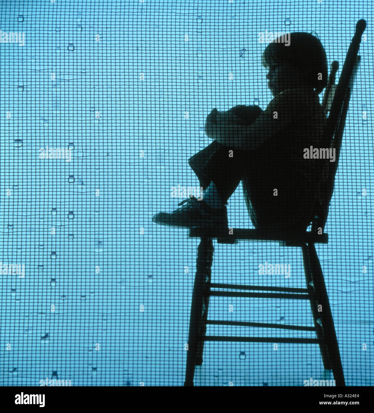 Young child sitting on a tall wooden chair as rain is falling on the