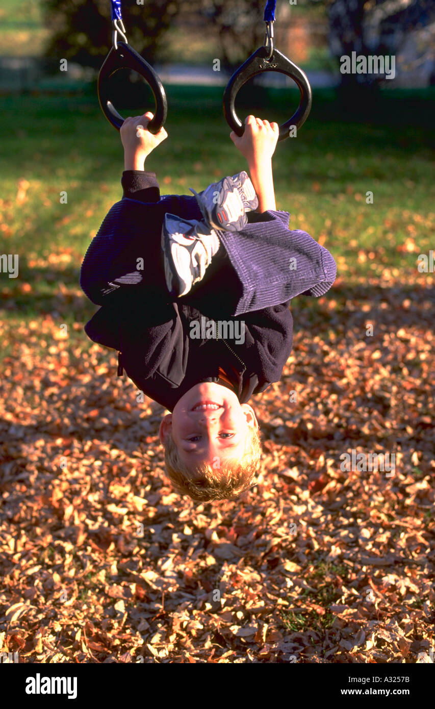 An eight year old boy smiles while hanging cross legged upside down from rings on a playground in Mount Horeb Wisconsin Stock Photo