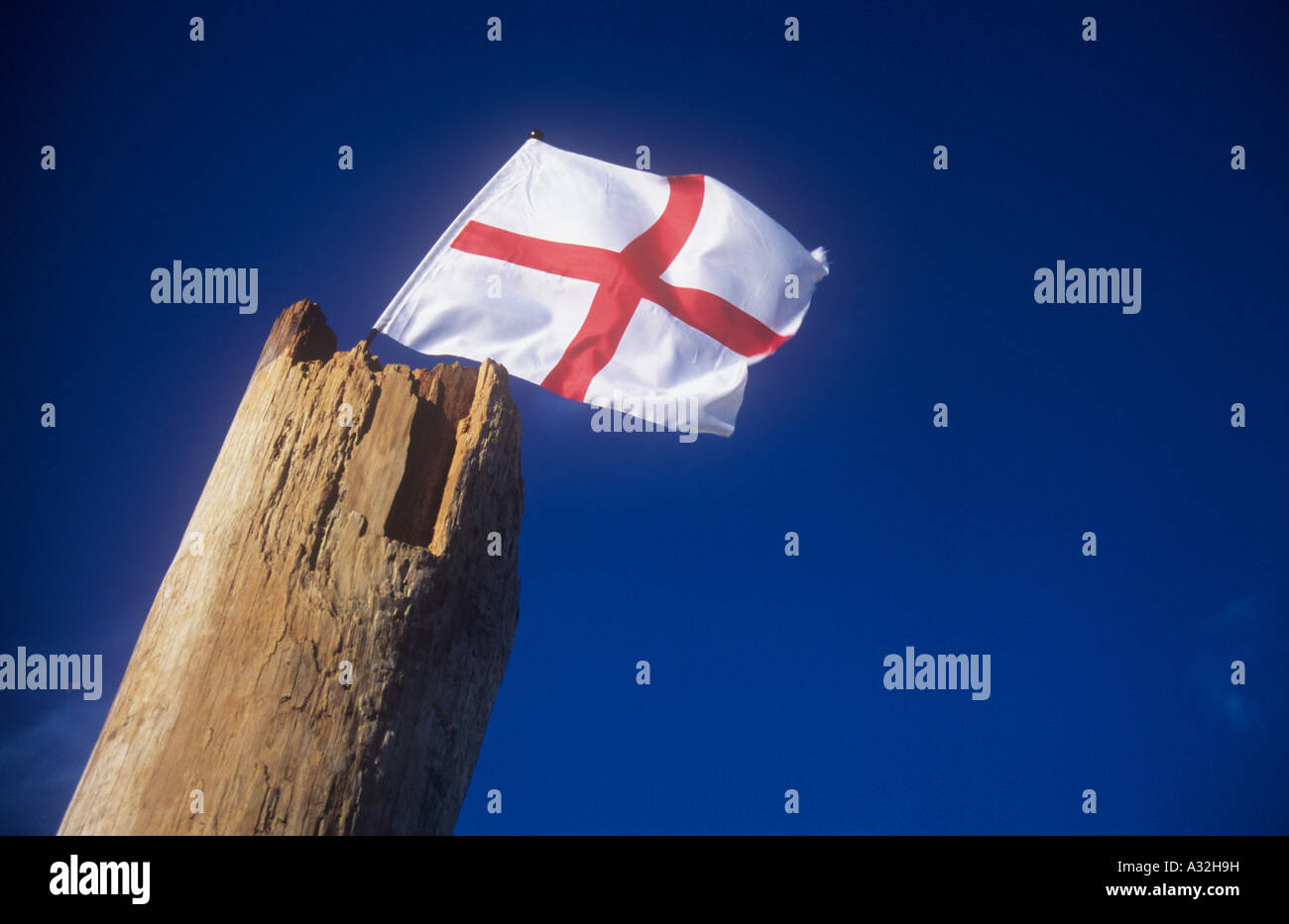 Small St George flag fixed in top of thick broken wooden pole and fluttering in warm evening light with deep blue sky Stock Photo