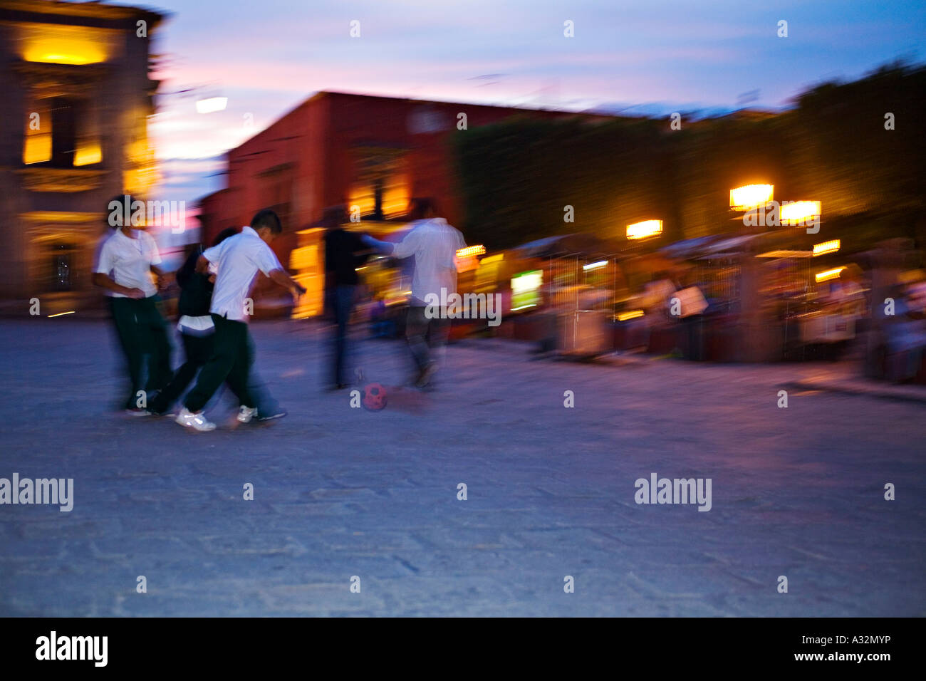 MEXICO San Miguel de Allende Children play soccer at dusk in plaza by el jardin cobblestones blurred motion of kids Stock Photo