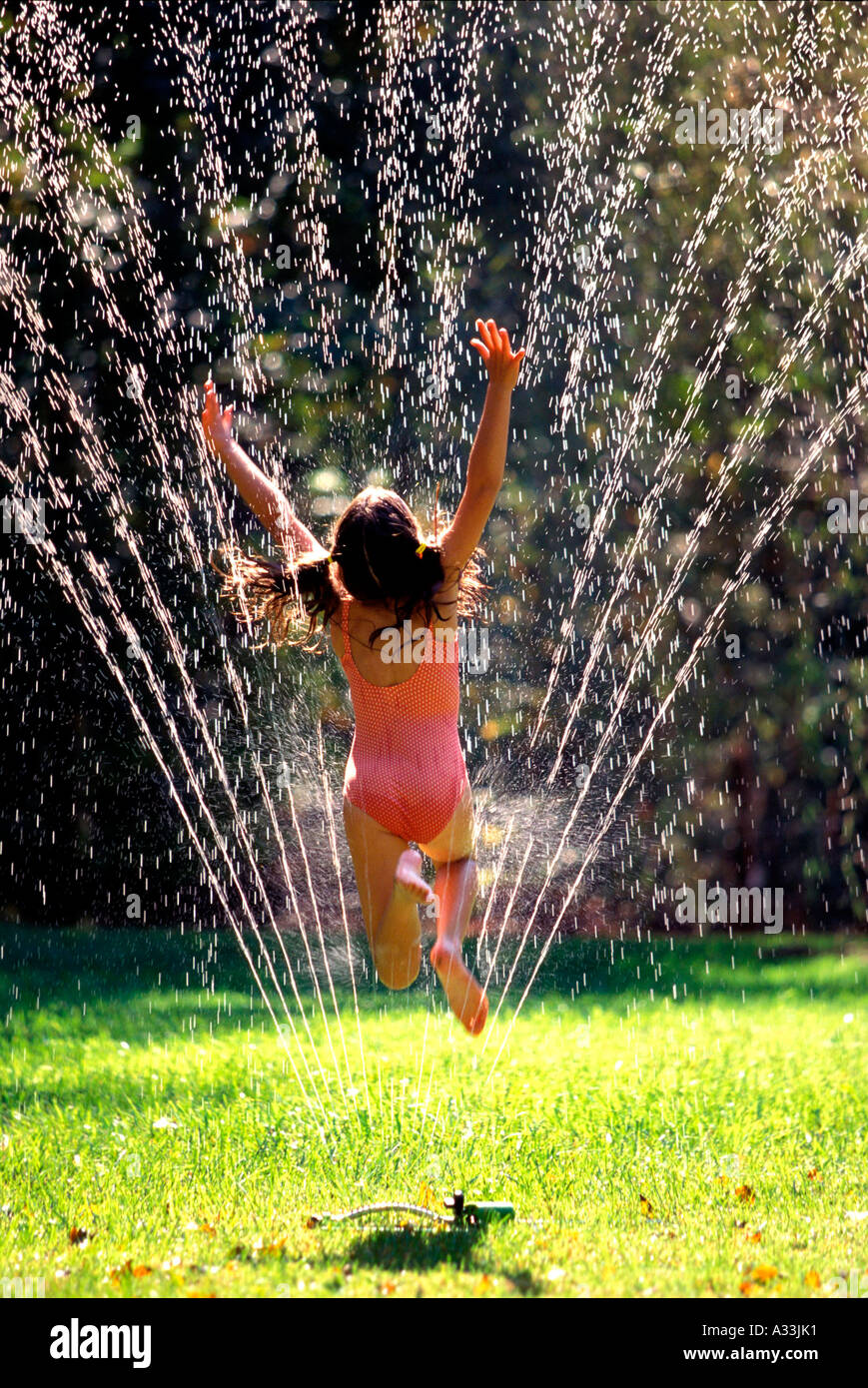 Girl jumps through sprinkler ABA Stock Photo