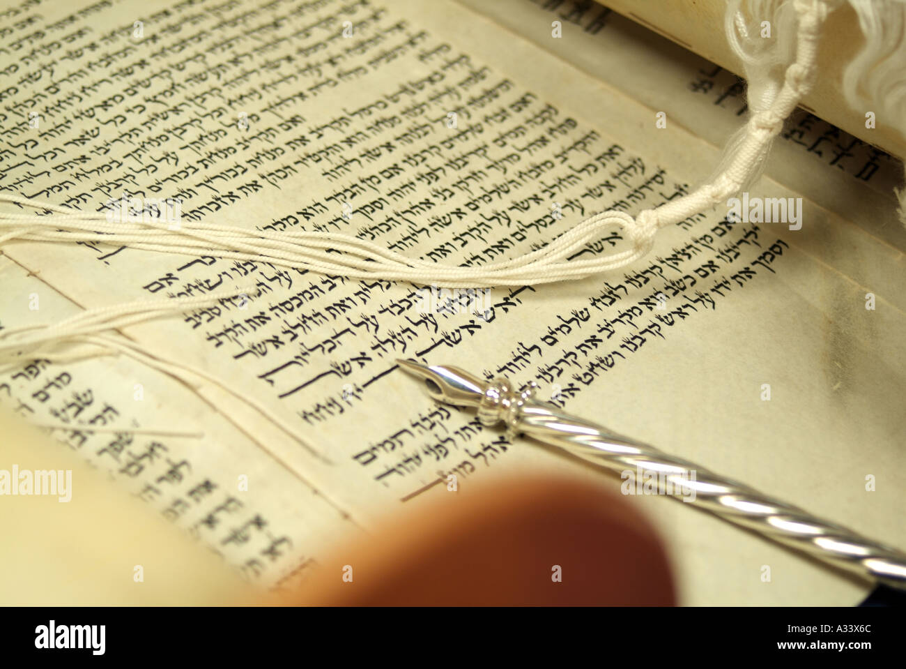 Hebrew Torah scroll with silver yad pointing to script and fridges of prayer shawl over text Stock Photo