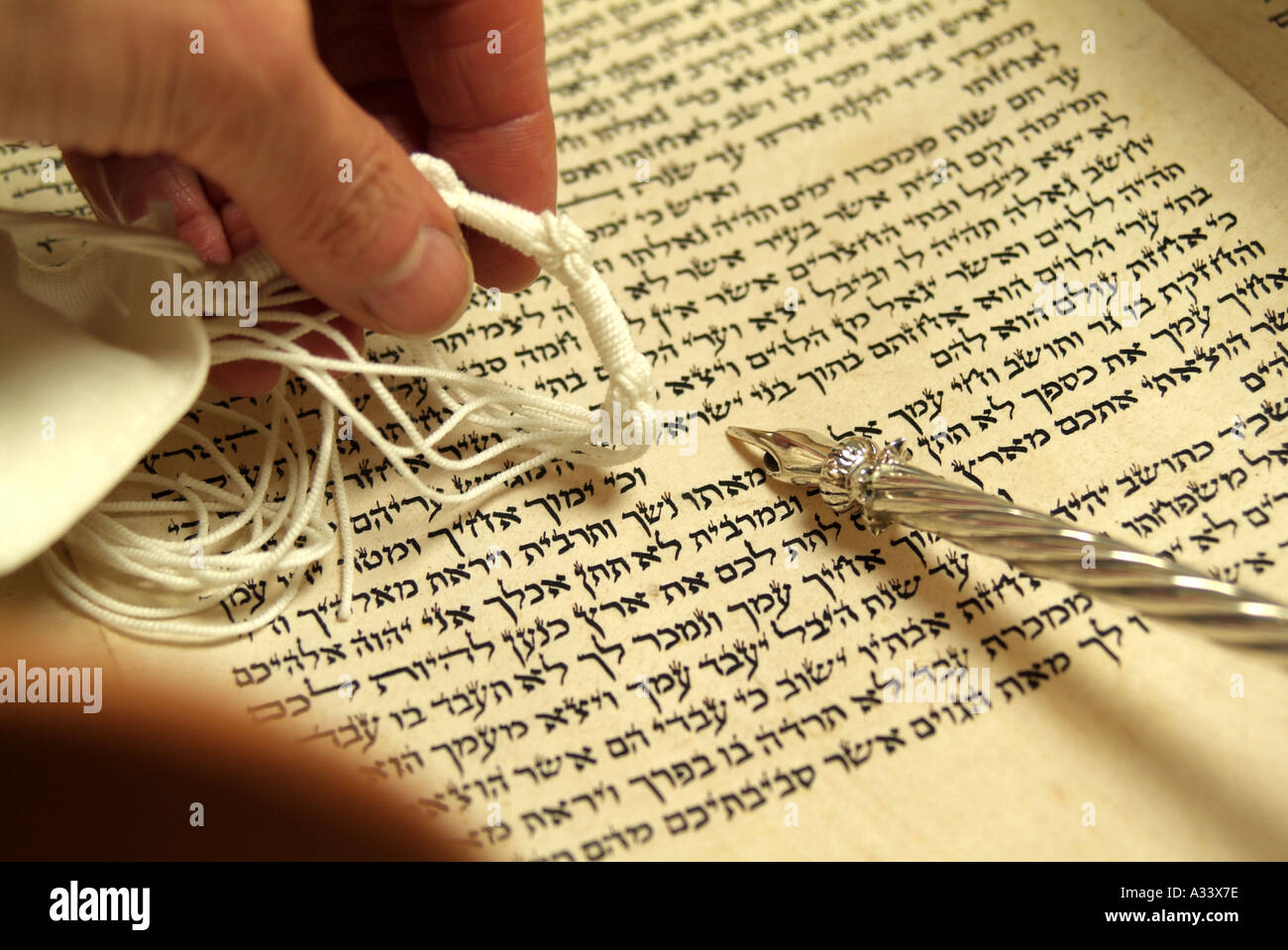 Hebrew Torah Scroll with silver yad (pointer) and prayer shawl (tallit) pointing to Hebrew letters and word Stock Photo