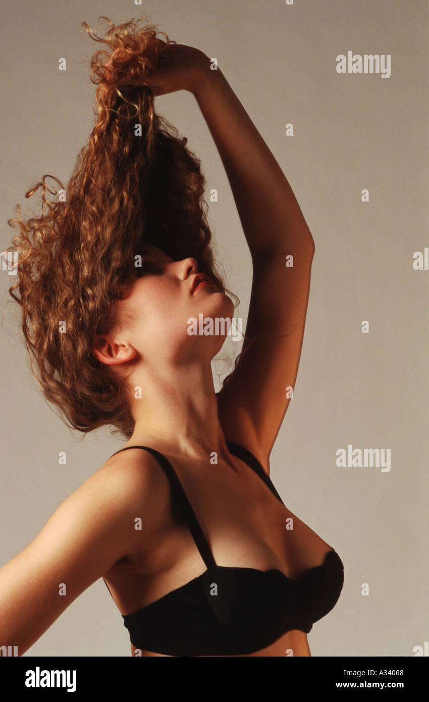 A young, sexy half naked woman of about 20, with long brown and curly hair  in a black bra, looking up and pulls here hair up Stock Photo - Alamy