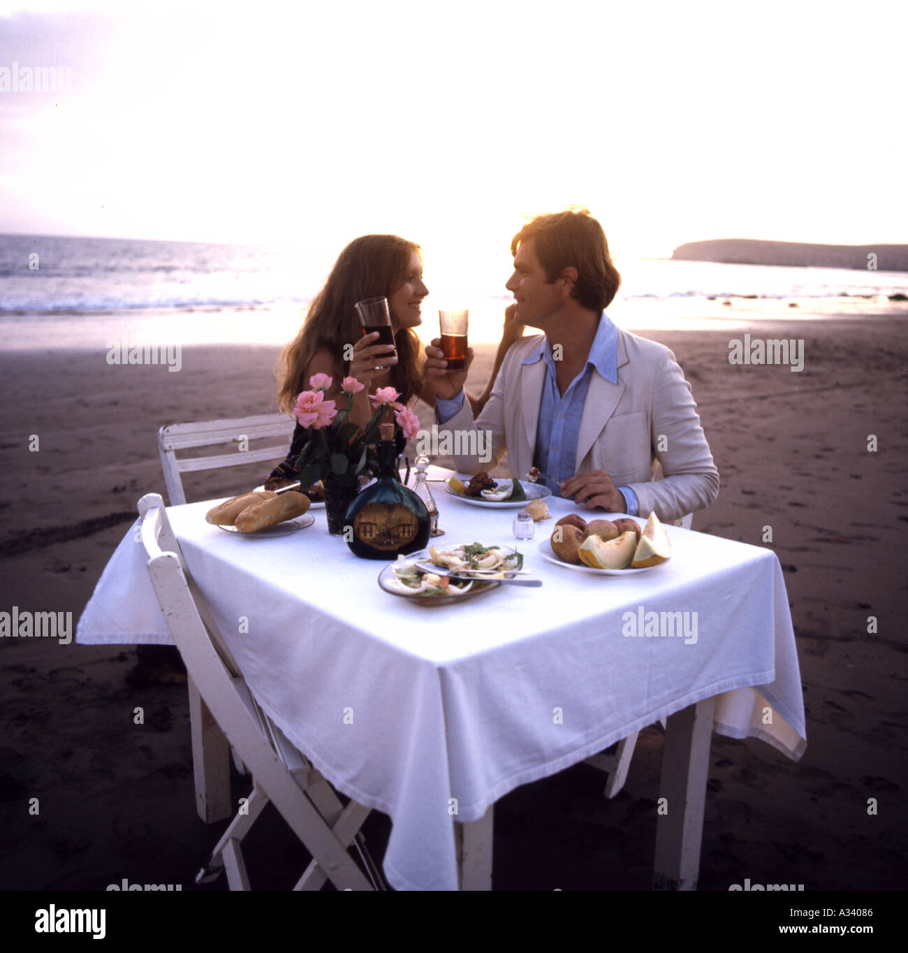 young couple in love, having dinner at sunset on the beach and drinking ...