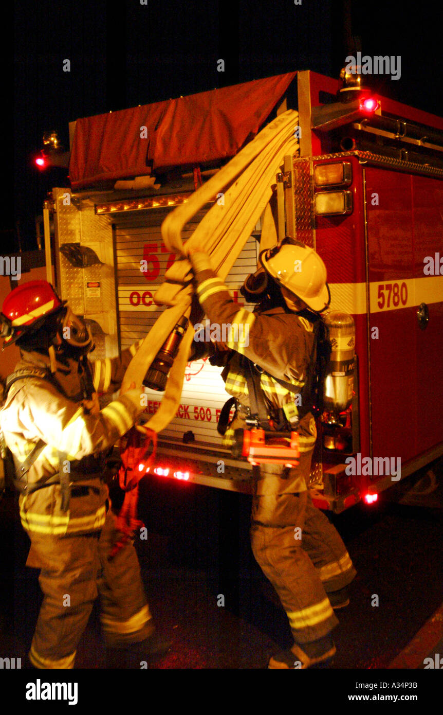 Two volunteer firefighters unload the rear skid load hoses off a fire engine in a nightime fire training exercise at Harmony School Occidental California USA Stock Photo