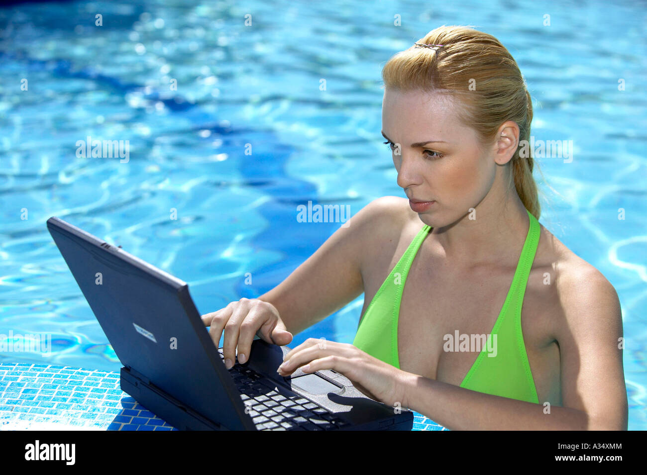 Blonde Frau arbeitet mit einem Laptop am Poolrand, blonde woman working on notebook at the edge of the pool Stock Photo