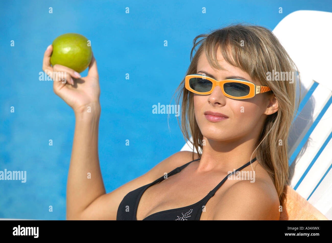 Frau isst Apfel am Pool, woman lying by the pool eating appel Stock Photo