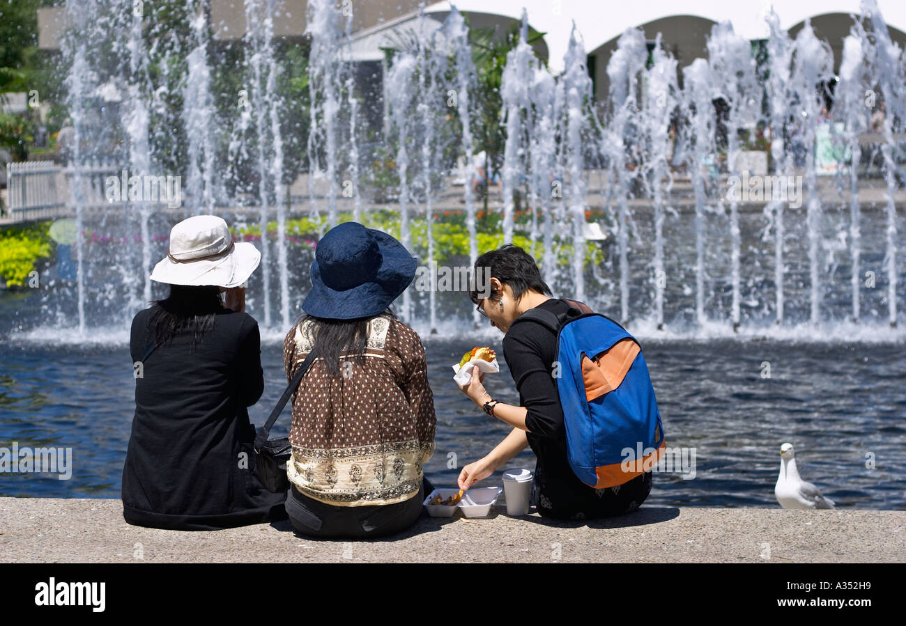 3 girlfriends having a break / lunch by the fountain. Summer outdoors, sunlit scene. Toronto, Ontario, Canada. Stock Photo
