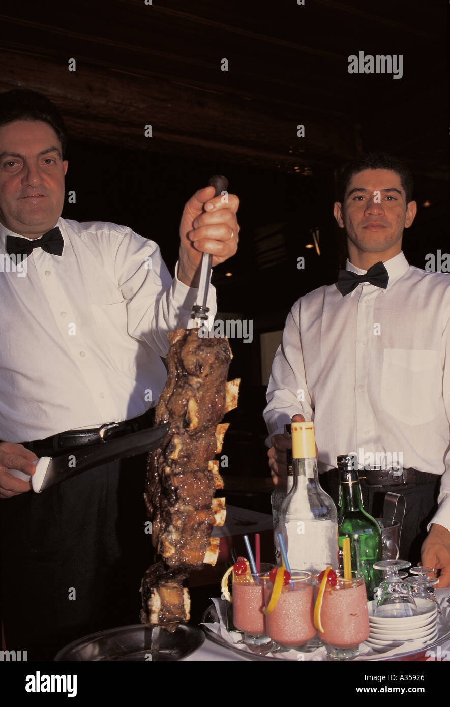 Rio de Janeiro Brazil Waiters slicing meat from a barbecue spit at a churrascaria barbecue house Stock Photo