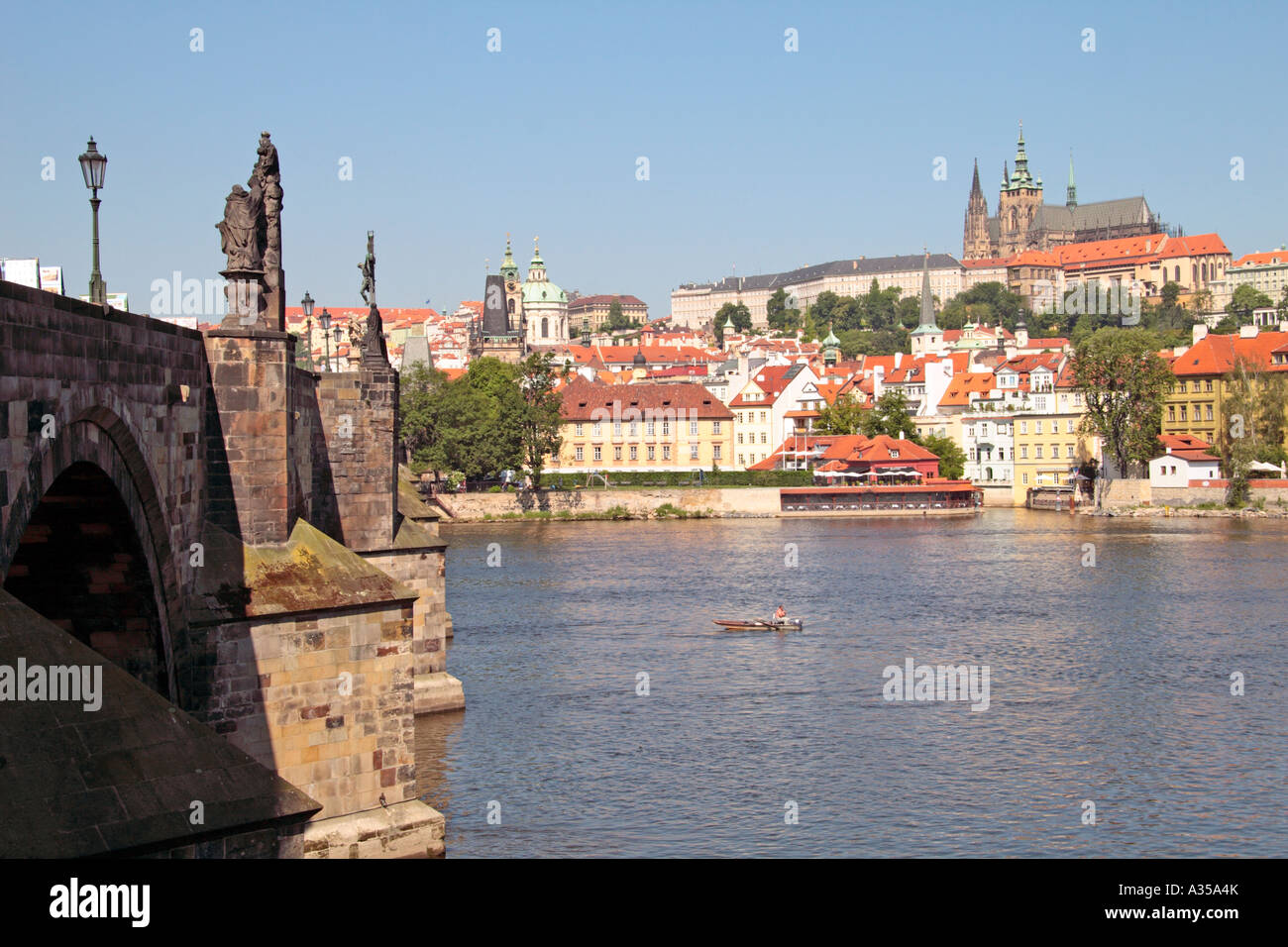 View of Prague Castle and St Vitus Cathedral over the Vltava river, with Charles Bridge and man fishing from boat Stock Photo