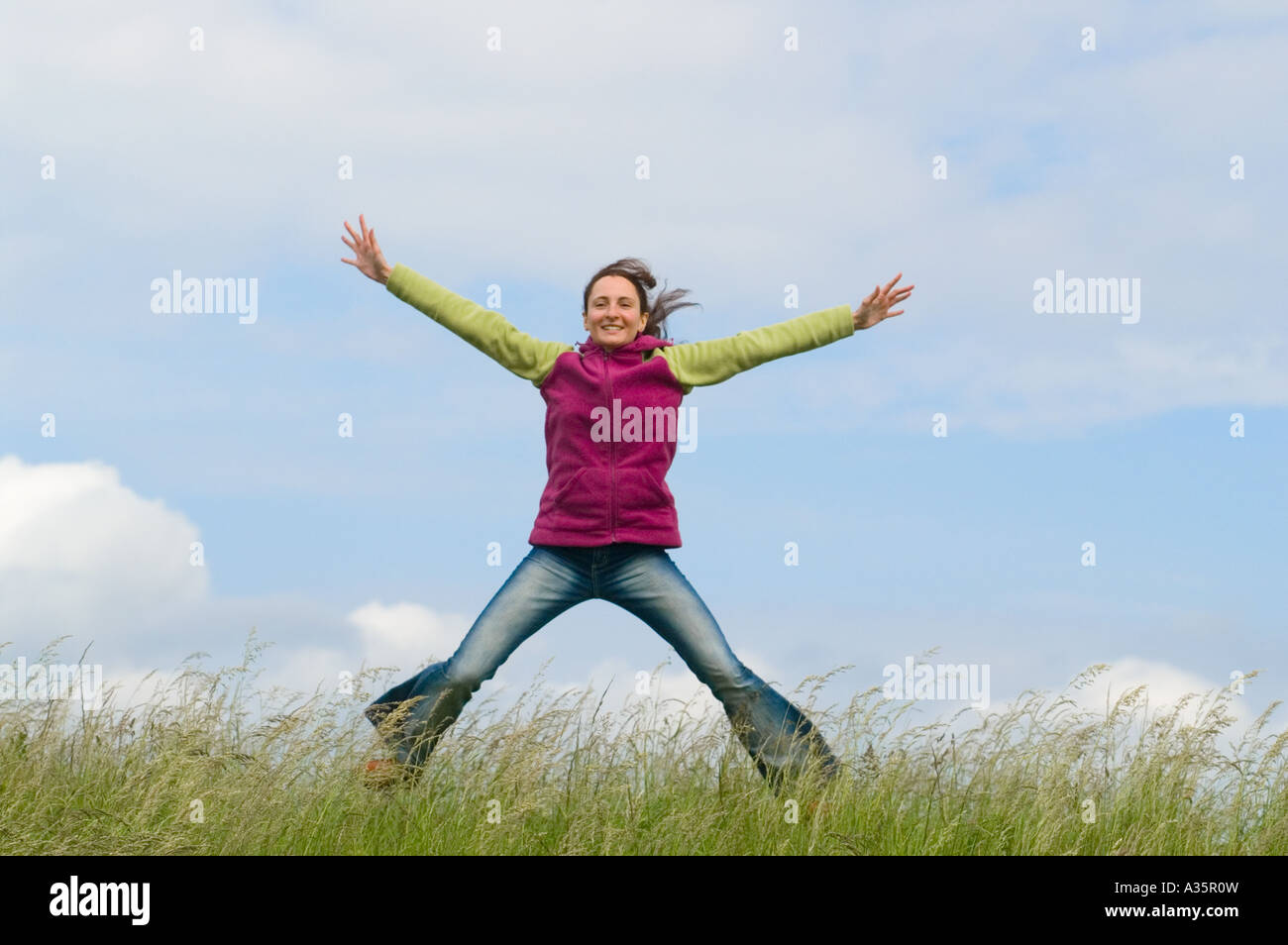 jumping young woman in the grass under a blue sky Stock Photo - Alamy