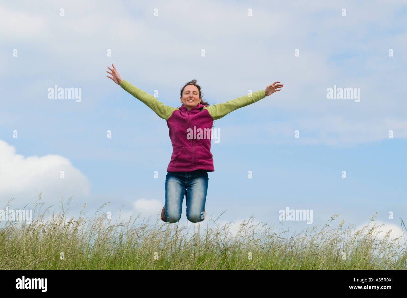 jumping young woman in the grass under a blue sky Stock Photo - Alamy