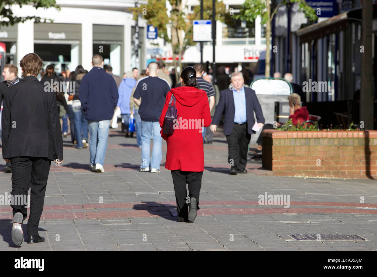 woman in red long coat walks along busy brick paved pedestrian precinct ...