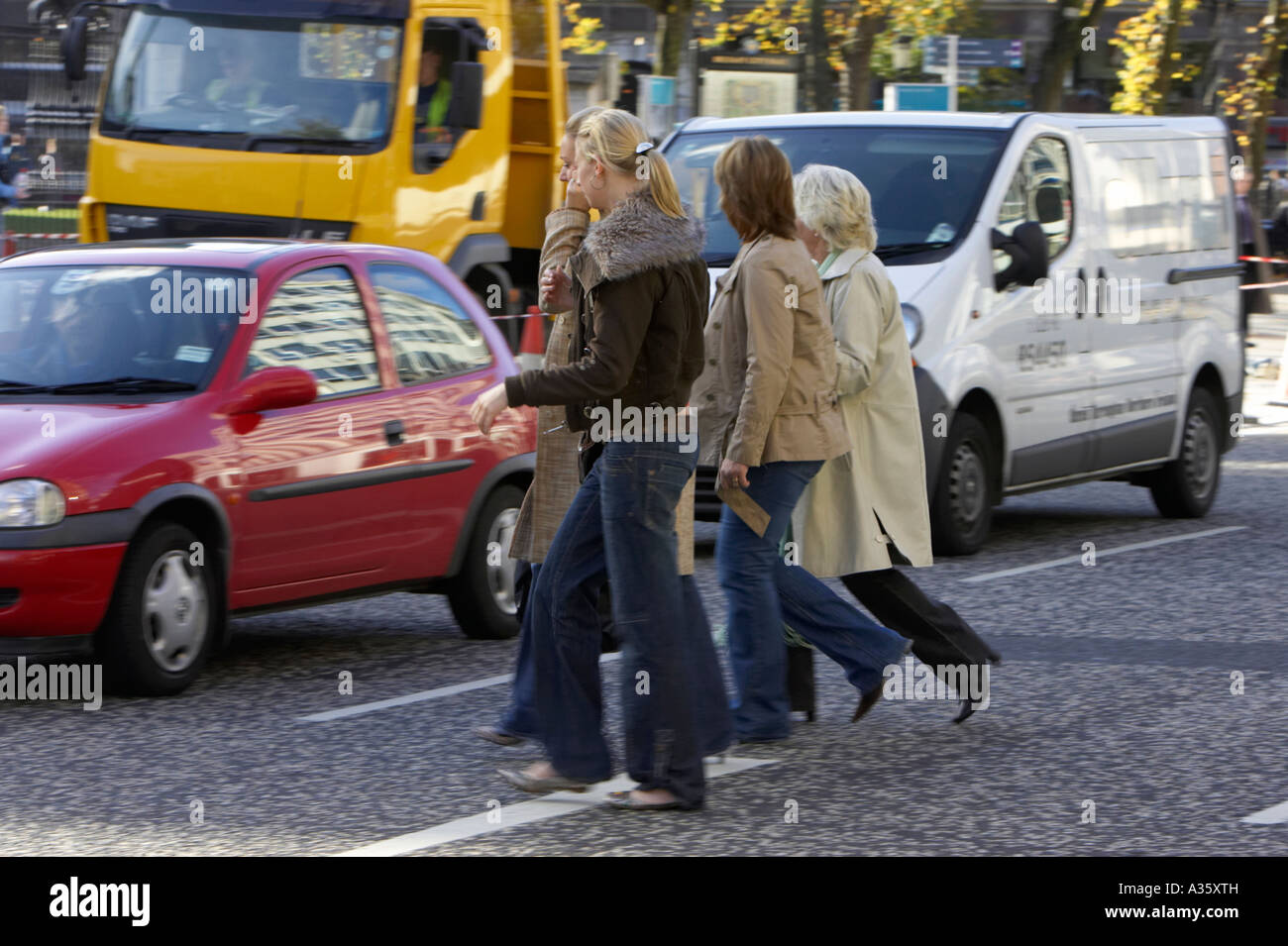 crowd of people women walking across the road through traffic in the middle of a road in a city centre Stock Photo