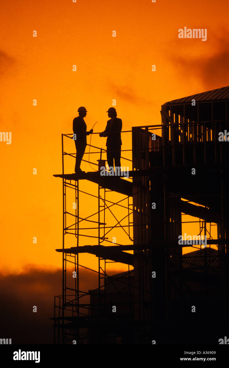 silhouette of two construction workers standing on high rise contruction scaffolding Stock Photo