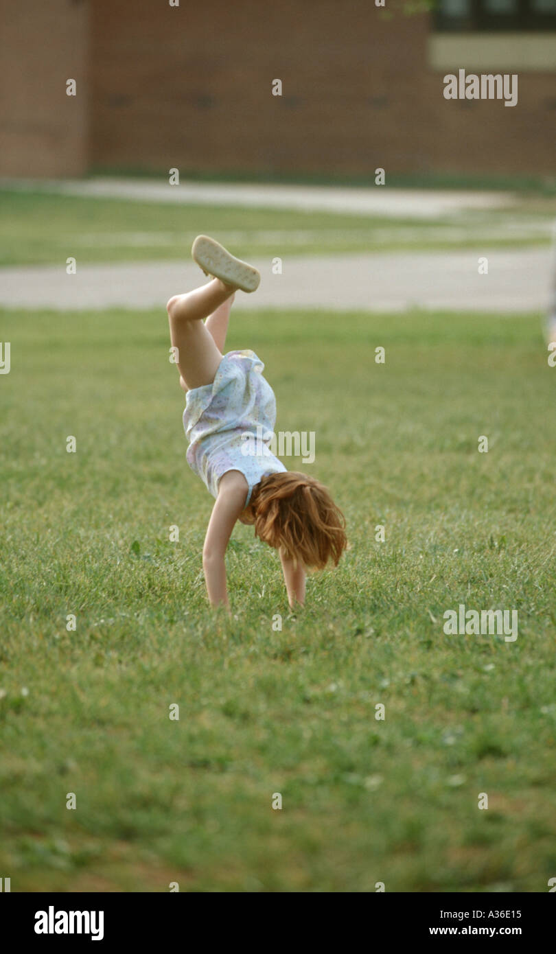 A young girl wearing a summer dress is doing a cartwheel in the green