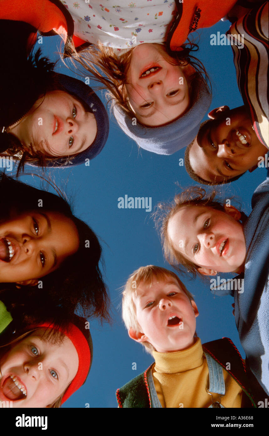 A group of racially diverse children are looking down at the viewer laughing as a deep blue sky hangs above them Stock Photo