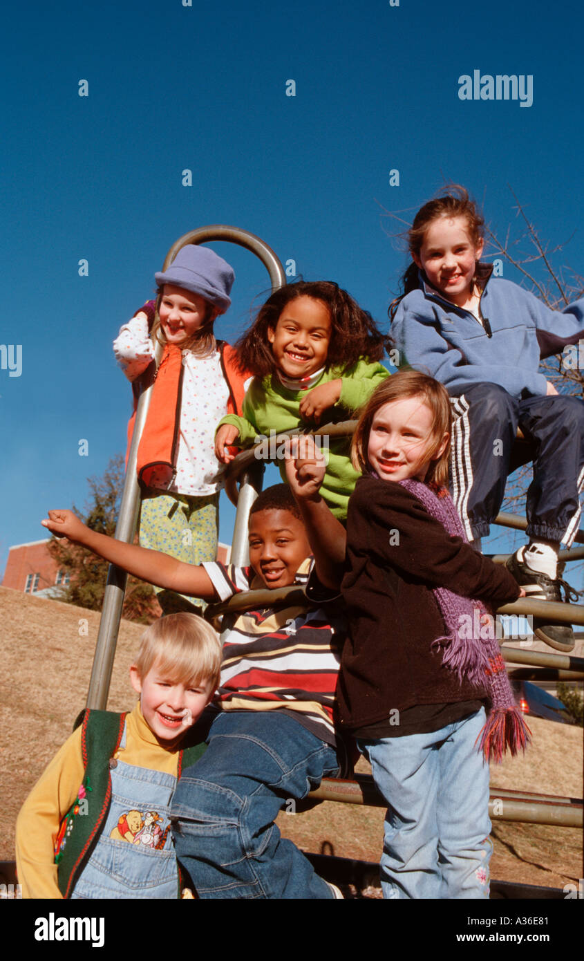 A group of racially diverse children are looking down at the viewer laughing while hanging from a play structure on a playground Stock Photo